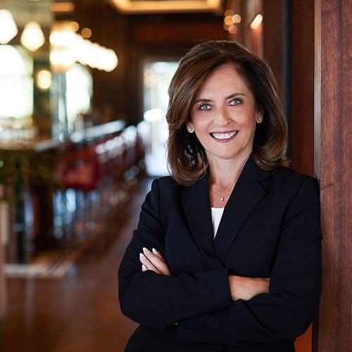 Professional woman smiling at camera with crossed arms wearing black blazer in modern interior setting