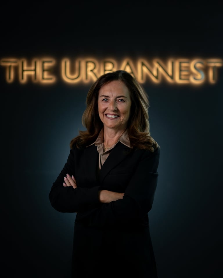 Professional woman in black blazer with arms crossed, smiling at camera in front of The Urbannnest glowing sign